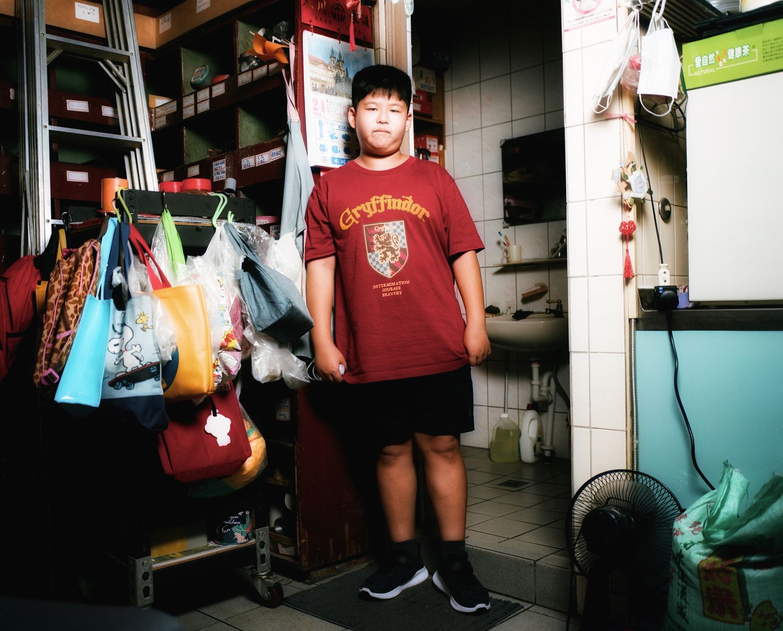 A boy is standing in front of a bathroom in Taiwan, reading in a Gryffindor T-shirt. Behind him...
